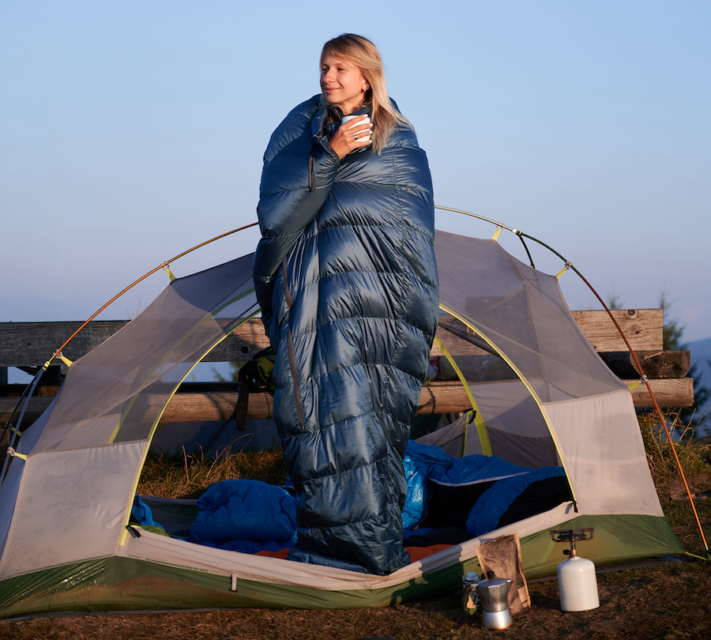 Frau steht im Schlafsack vor ihrem Zelt