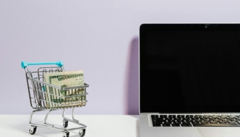 Compras en línea: un pequeño carrito de la compra junto a un ordenador portátil