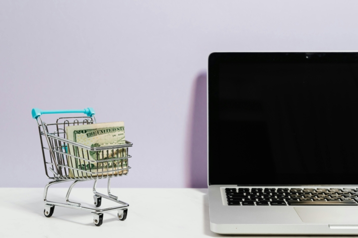 Online-Shopping: Kleiner Einkaufswagen neben einem Laptop