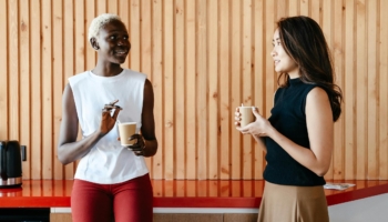 Two colleagues talk to each other over a cup of coffee